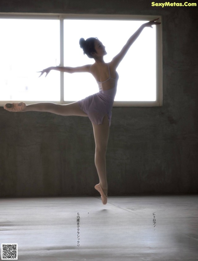 A young ballerina in a pink leotard and pointe shoes in front of a window.