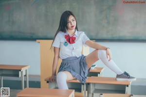 A woman in a school uniform standing in front of a blackboard.