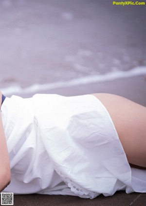 A woman in a white sweater leaning against a wall.