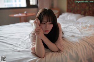 A woman sitting on a bed in a pink sweater.