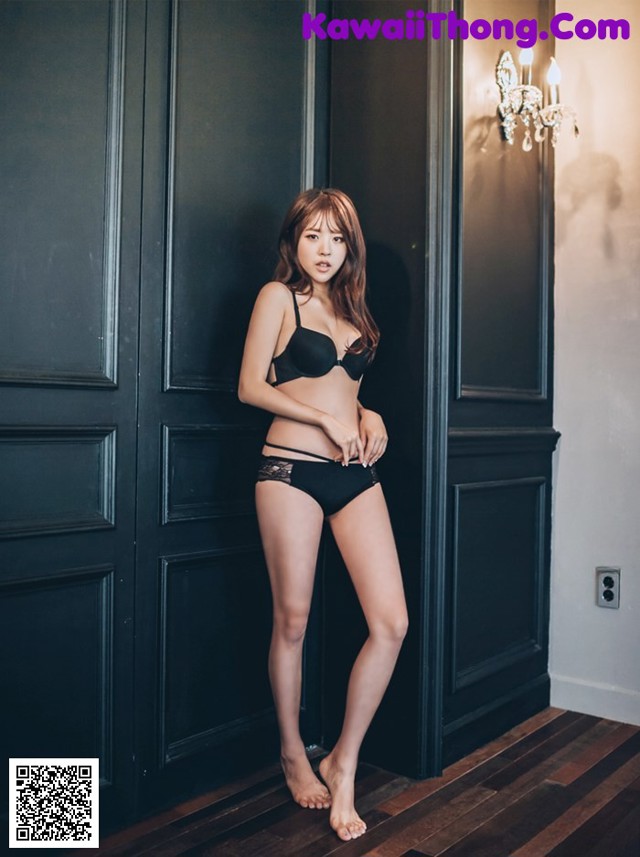 A woman in a black bra and panties standing in front of a door.