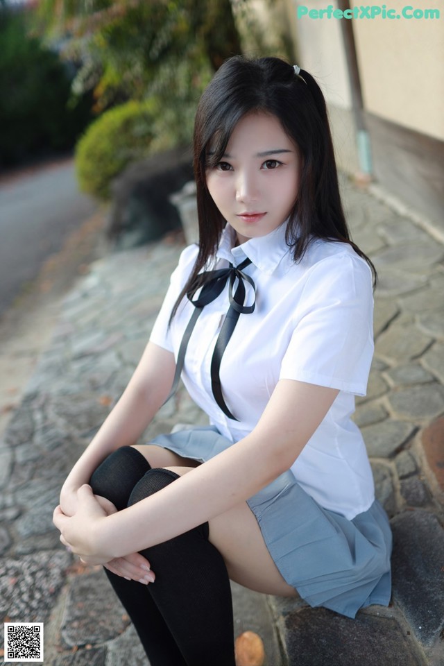 A woman in a school uniform sitting on a stone ledge.