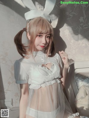 A woman in a white dress and bunny ears sitting on a bed.