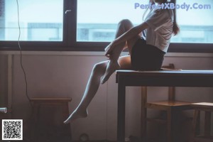 A woman sitting on a desk in front of a window.