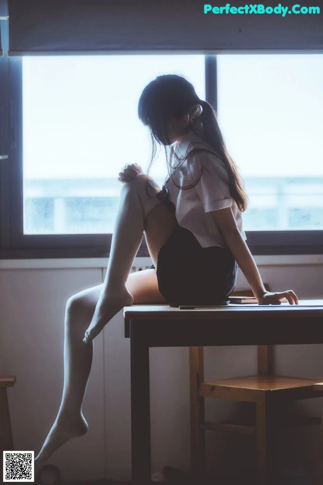 A woman sitting on a desk in front of a window.