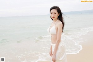 A woman in a white bikini sitting on the sand.