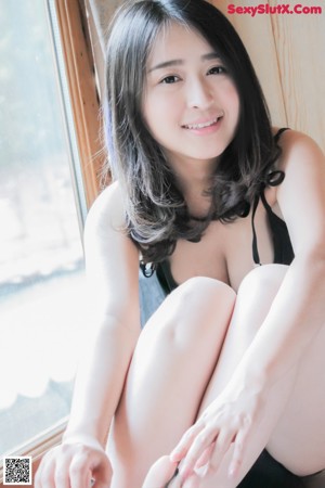 A woman in a blue swimsuit leaning against a tree.