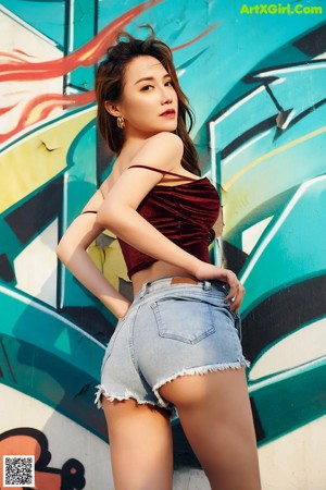 A woman in a red top and denim shorts posing for a picture.