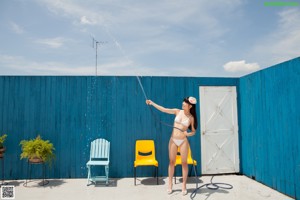 A woman in a white bikini standing next to a pink wall.