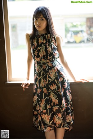 A woman in a floral dress standing in front of a window.