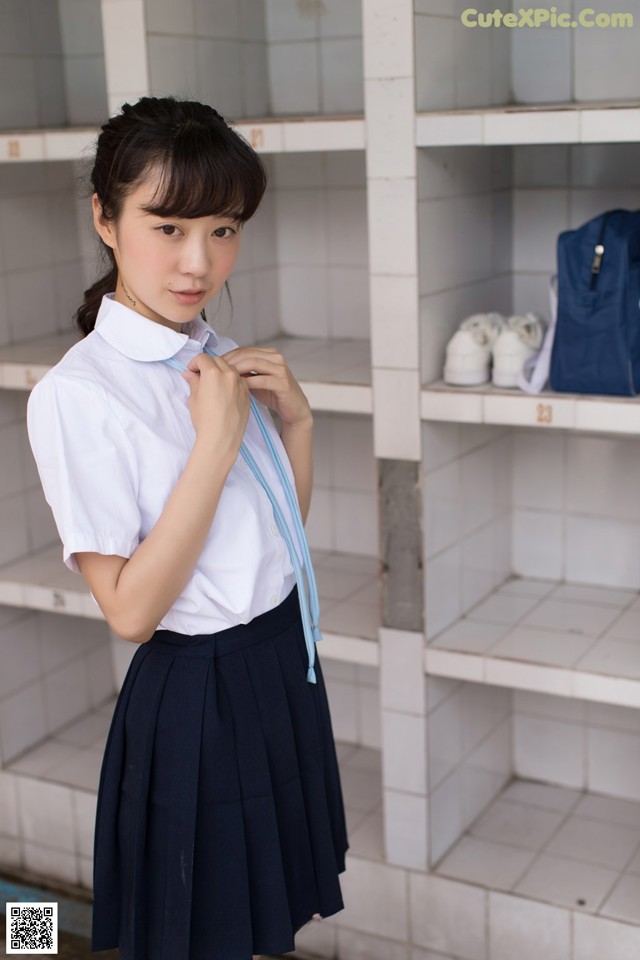 A woman in a school uniform standing in front of a locker.