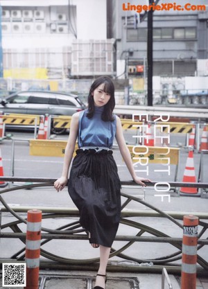 A woman standing in front of a window wearing a blue skirt.