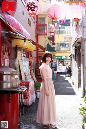 A woman in a pink dress standing next to a large metal pot.