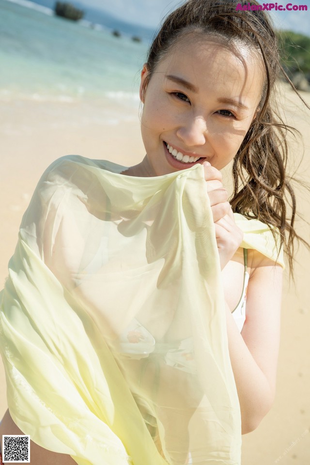A woman in a bikini holding a yellow scarf on the beach.