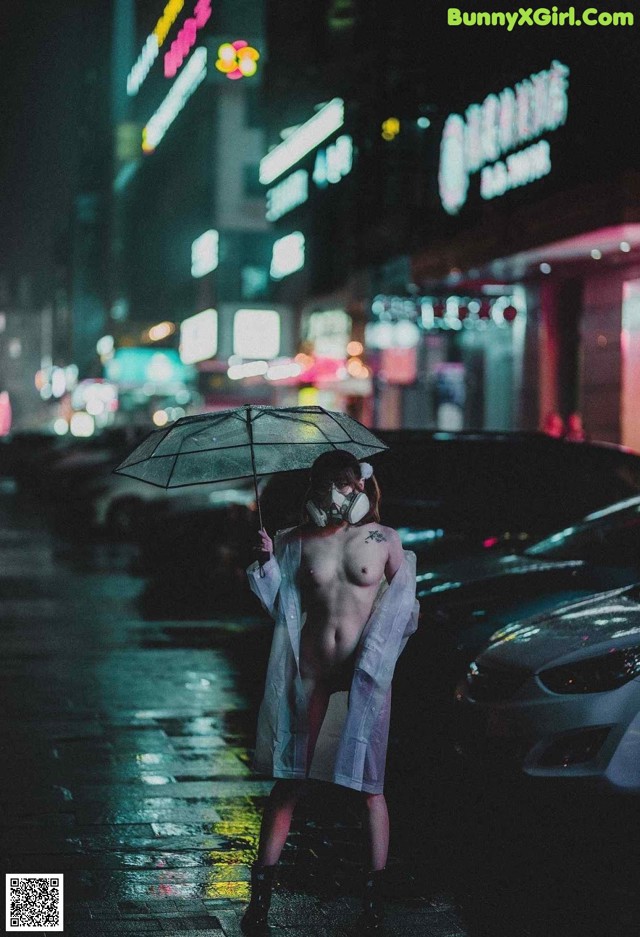 A naked woman in a white coat holding an umbrella in the rain.