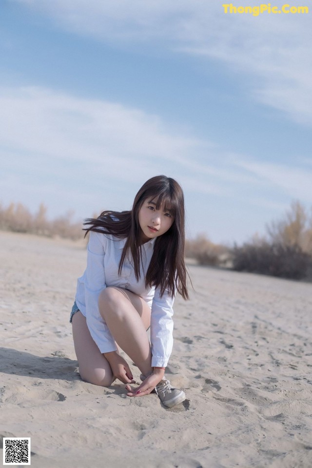 A woman kneeling on a sandy beach with her legs crossed.